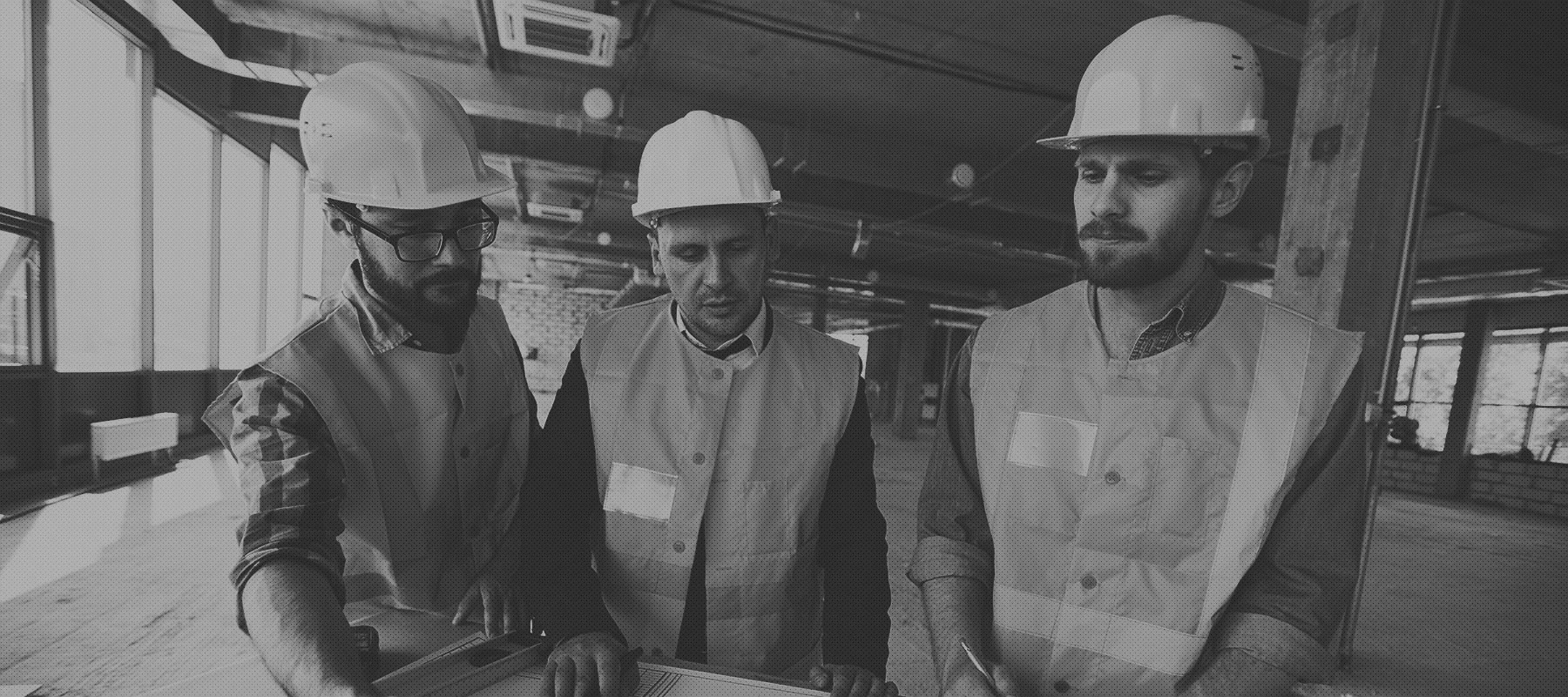 Three men in hard hats and vests looking at a piece of paper.